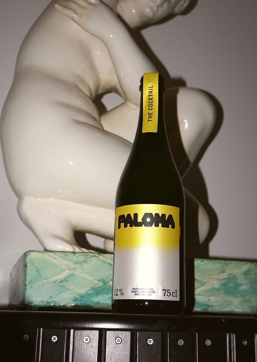 Flasche Paloma mit gelbem Etikett vor einer Porzellanfigur
